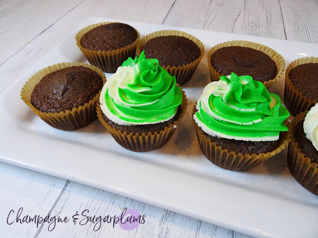 Icing chocolate cupcakes with white and green frosting on a white plate by Champagne and Sugarplums