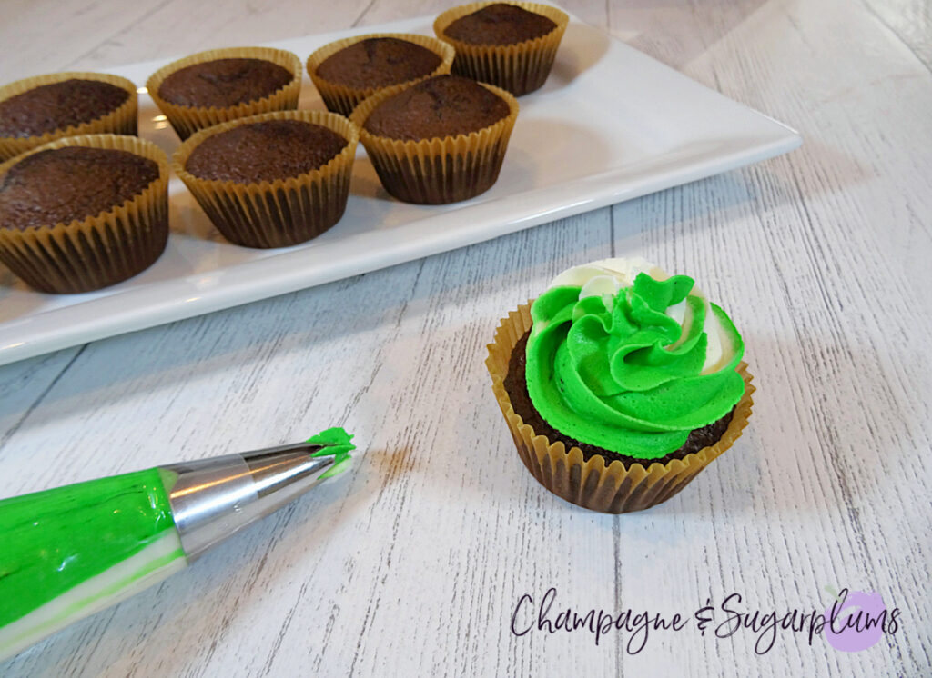 Icing chocolate cupcakes with white and green frosting on a white plate by Champagne and Sugarplums