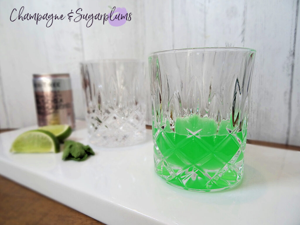 Cucumber Mint Cocktail on a white plate, beside lime slices, mint leaves and a can of club soda by Champagne and Sugarplums