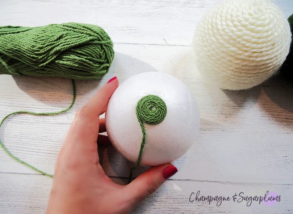 Wrapping green yarn around a  Styrofoam ball on a white background by Champagne and Sugarplums