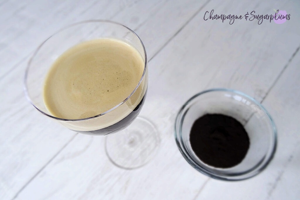Garnishing a cocktail with coffee grounds, beside a bowl of grounds on a white background by Champagne and Sugarplums