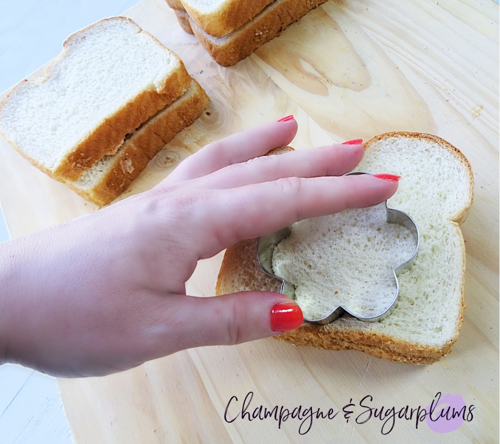 Cutting flower shapes into chicken sandwiches on a wood board by Champagne and Sugarplums