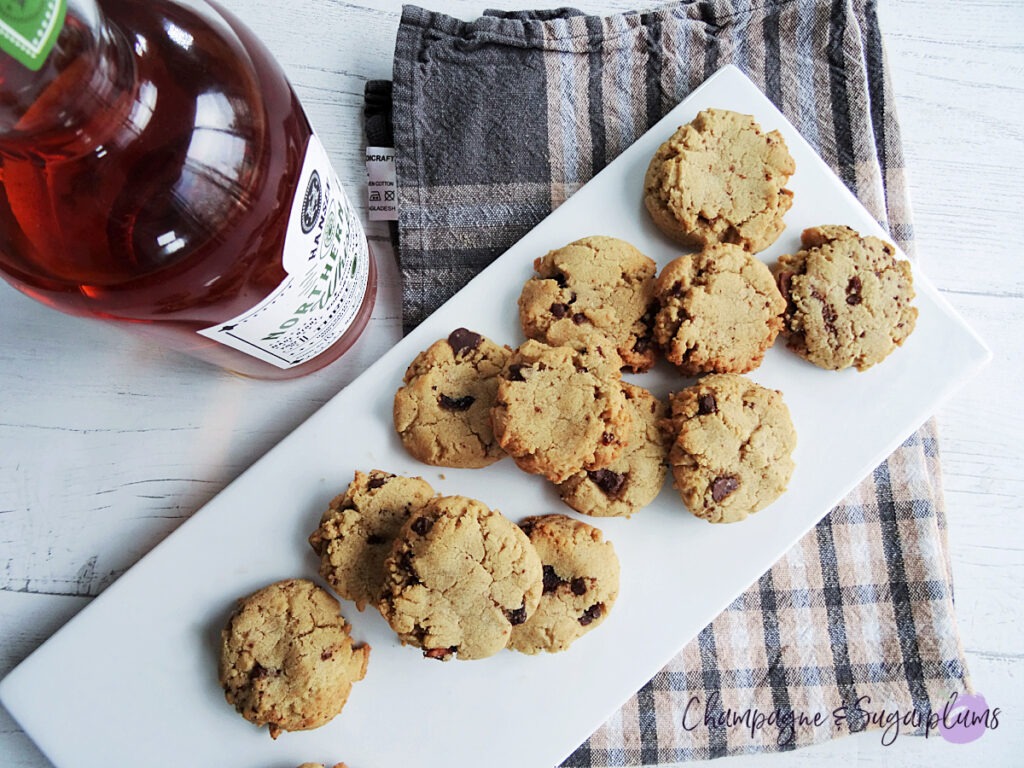 Whiskey Bacon Chocolate Cookies on a white plate, with a bottle of whiskey and a plaid tea cloth on a white background by Champagne and Sugarplums