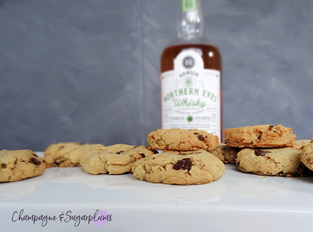 Whiskey Bacon Chocolate Cookies on a white plate, with a bottle of whiskey on a grey background by Champagne and Sugarplums