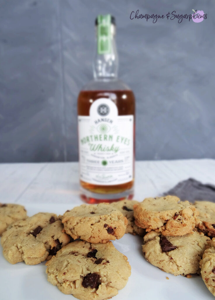 Whiskey Bacon Chocolate Cookies on a white plate, with a bottle of whiskey and a plaid tea cloth on a white background by Champagne and Sugarplums