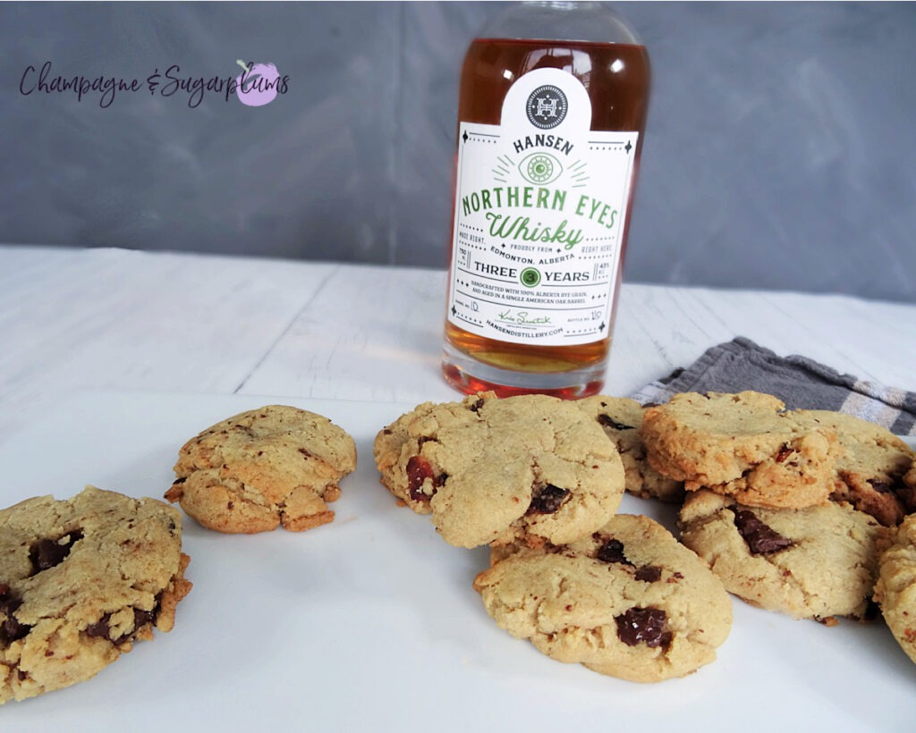 Whiskey Bacon Chocolate Cookies on a white plate, with a bottle of whiskey and a plaid tea cloth on a white background by Champagne and Sugarplums