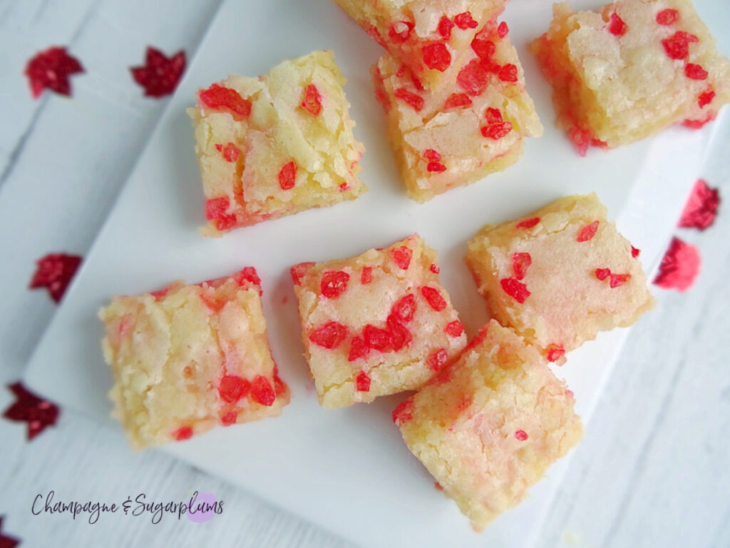 Canada Day Brownies on a white plate with red maple leaf confetti scattered around by Champagne and Sugarplums