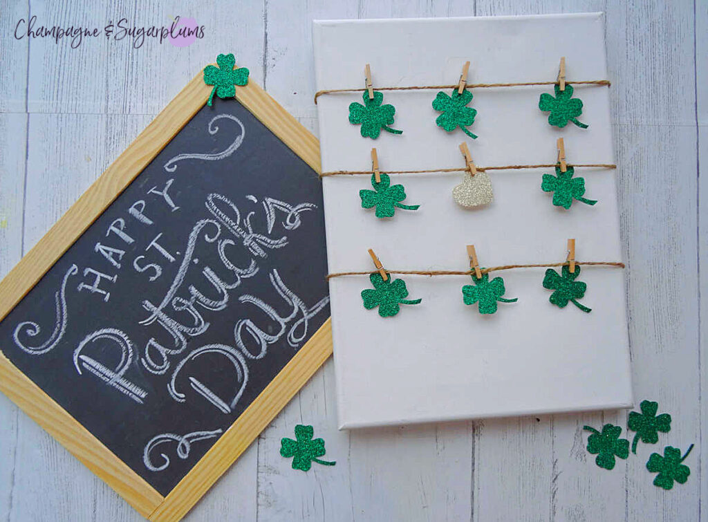 Completed clover canvas on a white background, with green clover cut-outs sprinkled around, beside a small slate that says 'Happy St. Patrick's Day' by Champagne and Sugarplums