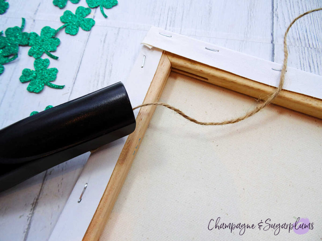Using a stapler to attach twine to the back of a white canvas by Champagne and Sugarplums