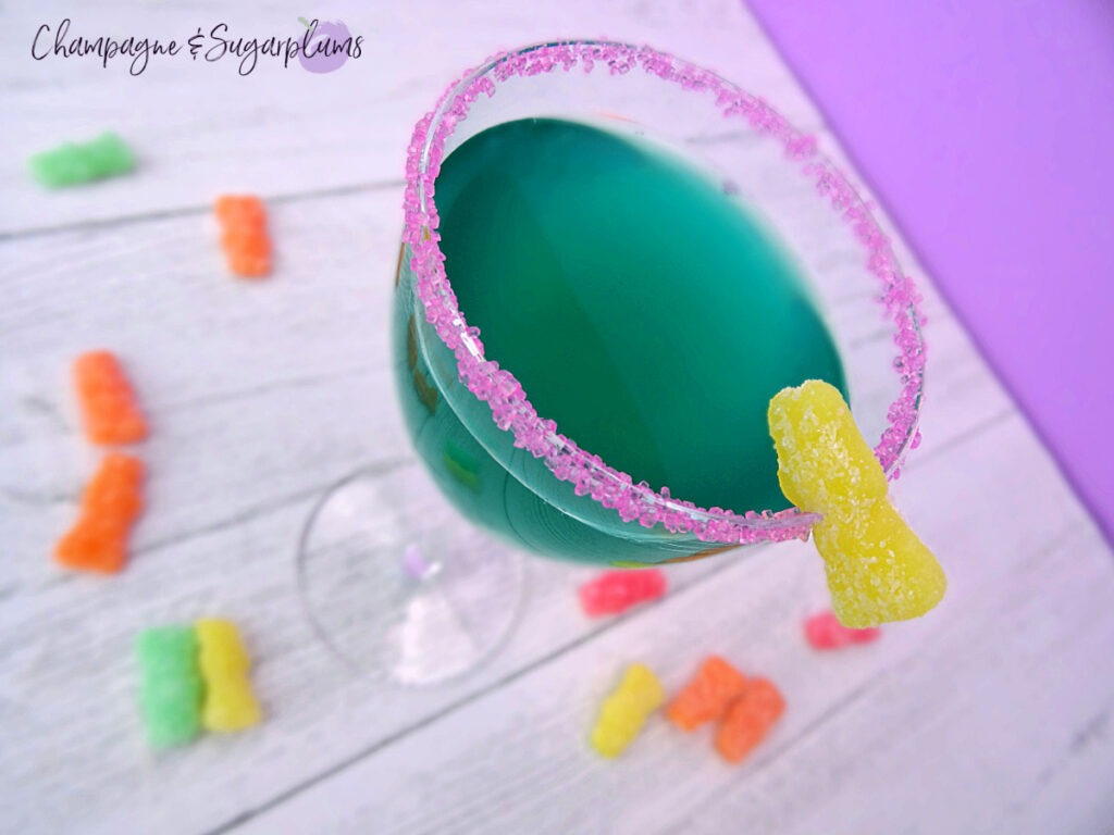A Tipsy Bunny cocktail in a Nick and Nora glass on a white and purple background with sour candies by Champagne and Sugarplums