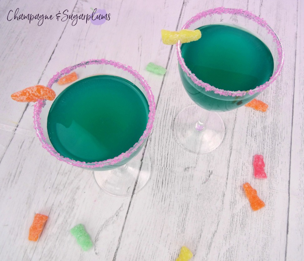 Two tipsy bunny Easter Cocktail in Nick and Nora glasses on a white background with sour candies by Champagne and Sugarplums