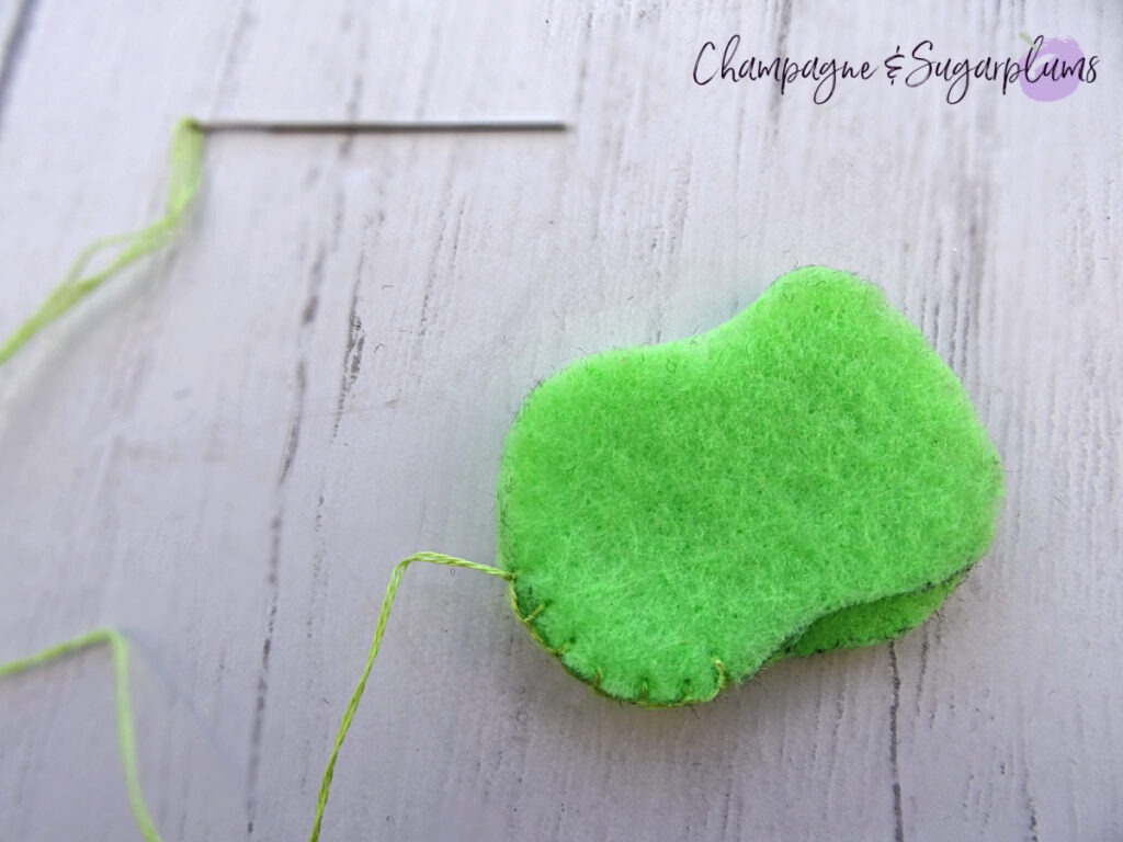 Stitching the edges of a felt green apple on a white background by Champagne and Sugarplums