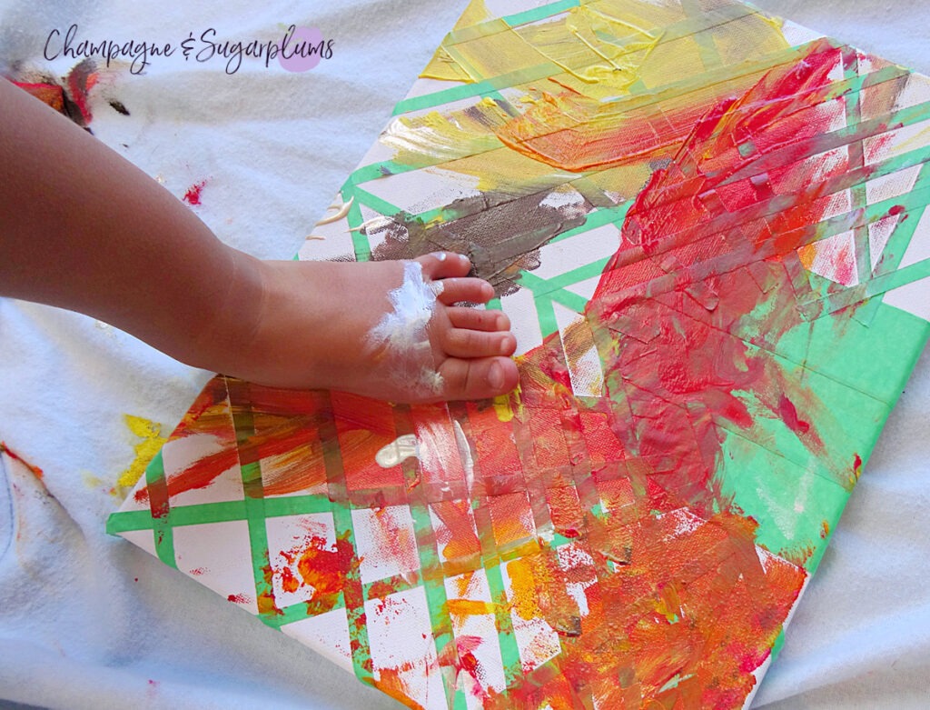 Fall colours being painted in a geometric pattern on a canvas by a toddler by Champagne and Sugarplums
