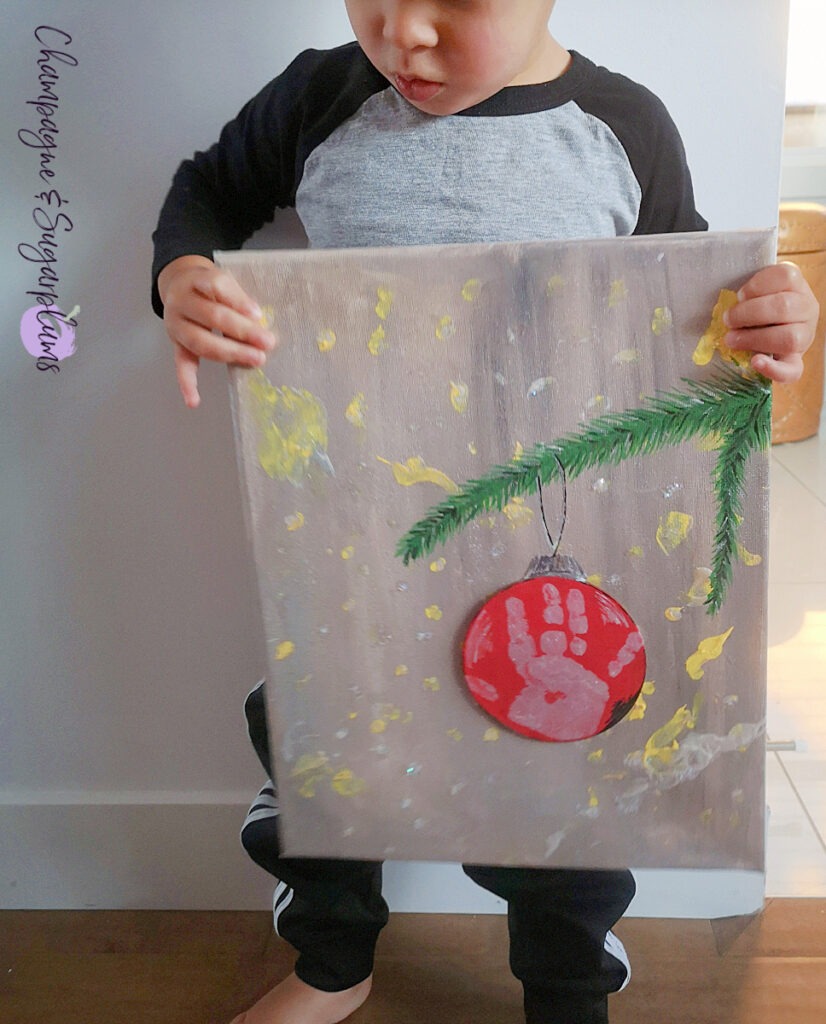 Handprint Christmas Art being held by a toddler by Champagne and Sugarplums