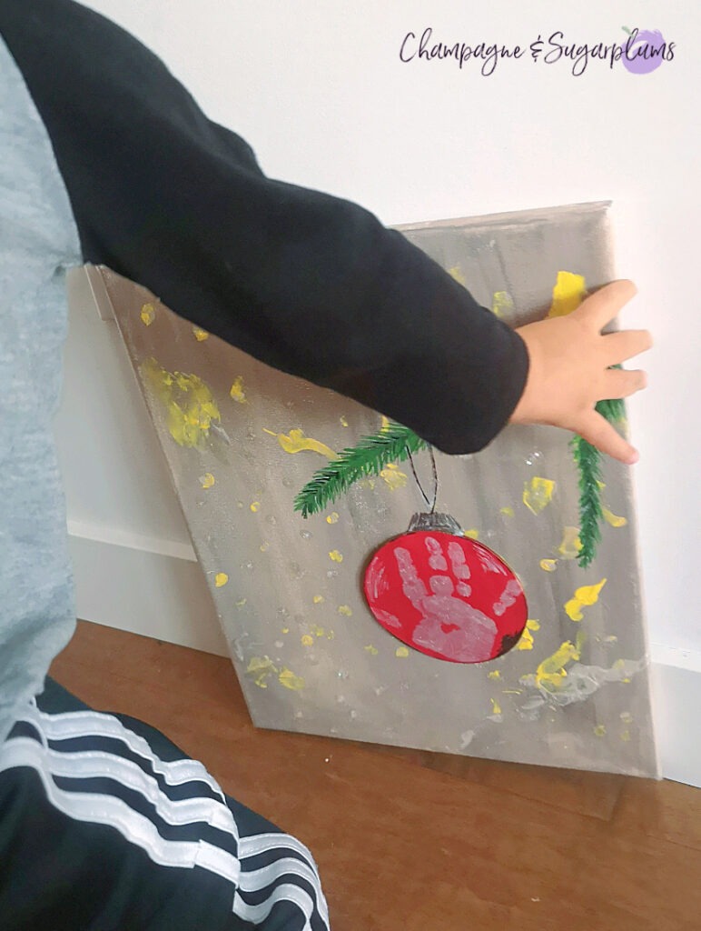 Handprint Christmas Art being held by a toddler by Champagne and Sugarplums