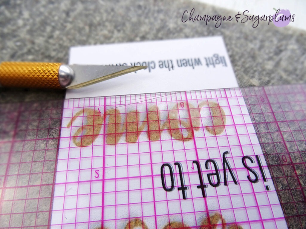 Cutting a small slit into a printed black and gold card on a white background by Champagne and Sugarplums